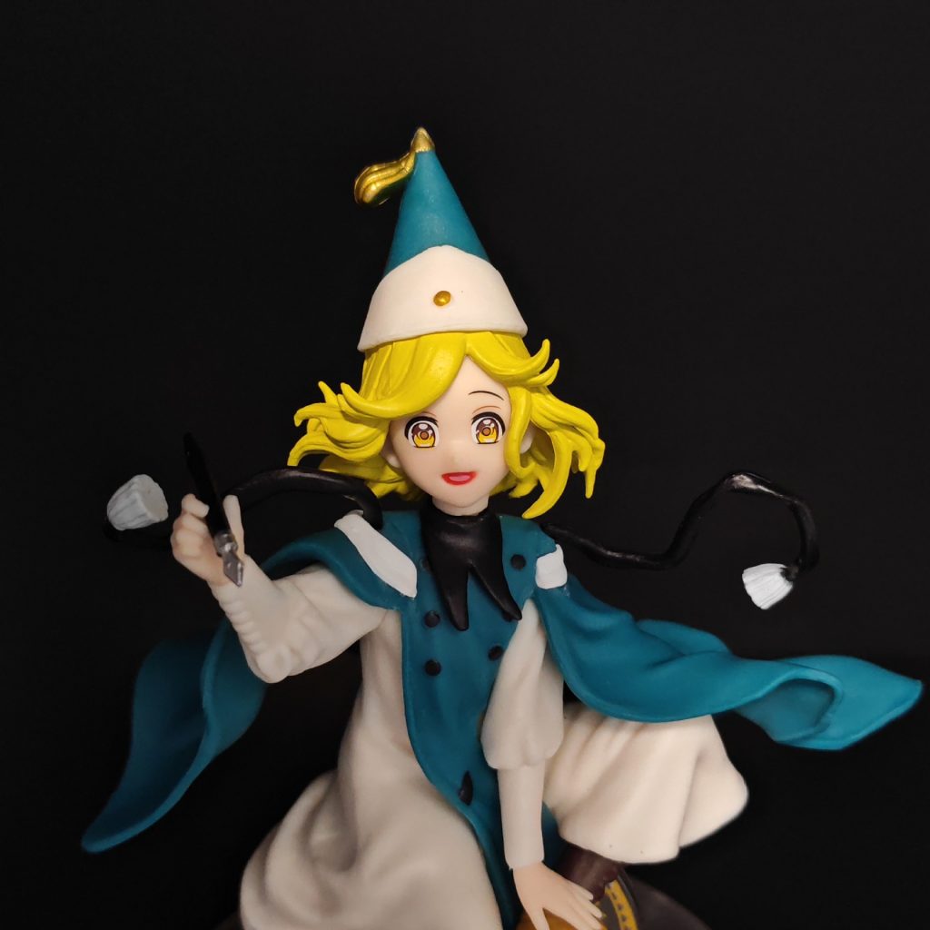Close-up of Coco figurine's pointed teal hat, blonde hair, face and drawing pen