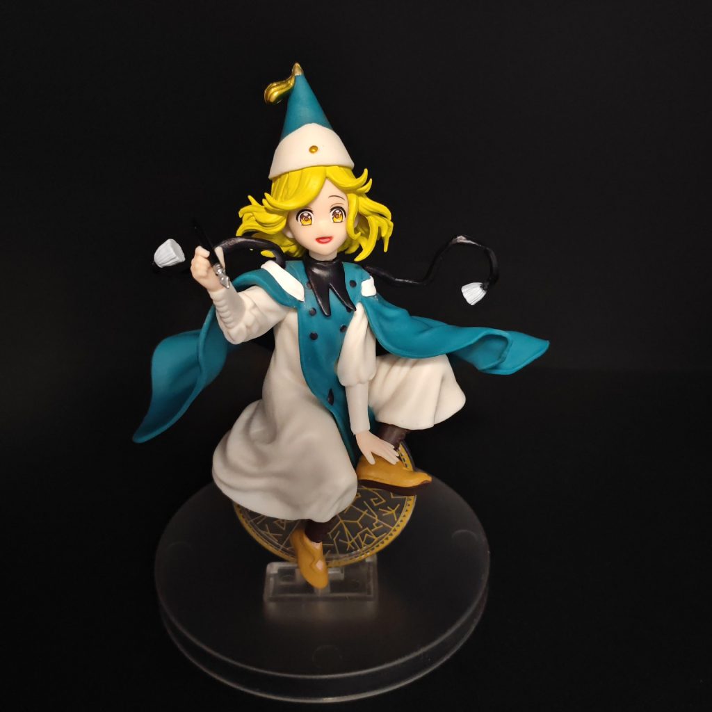 Coco figurine with pointed hat, flowing teal cape and round base, front view