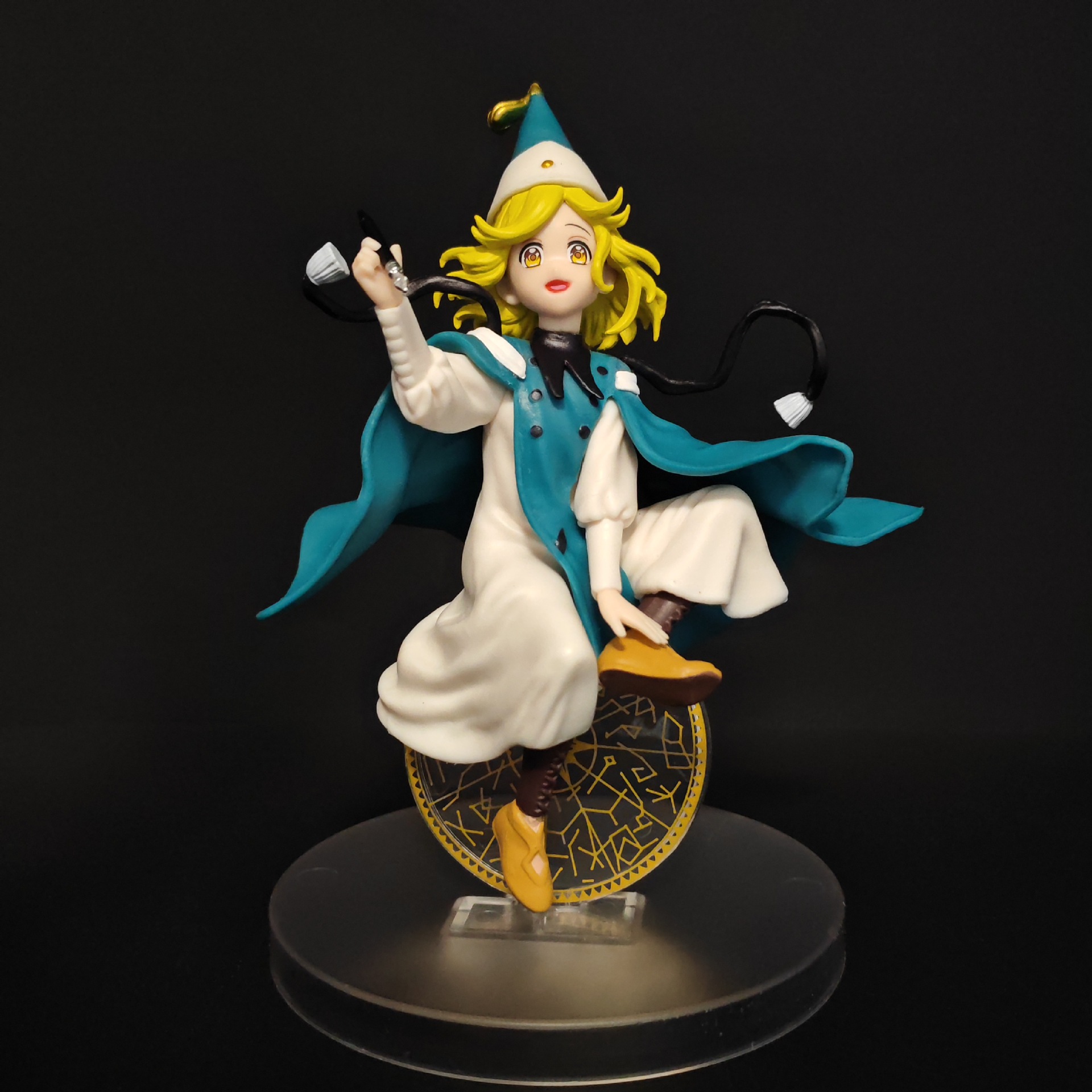 Three-quarter front view of Coco figure with raised pen, circular motif and round base