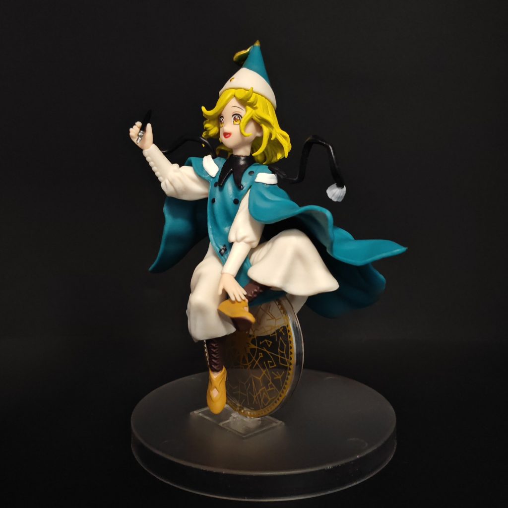 Side view of Coco figurine with teal cape and circular gold-patterned backdrop