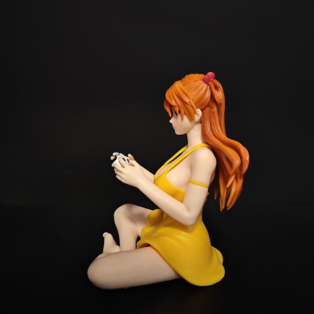 Left profile of seated Asuka figure showing her orange hair and yellow dress