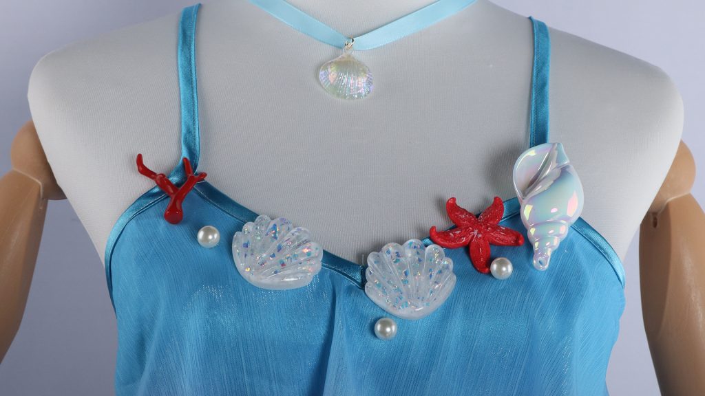 Dolia costume neckline detail with blue straps, shell and coral trim, and shell pendant