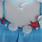 Dolia costume neckline detail with blue straps, shell and coral trim, and shell pendant