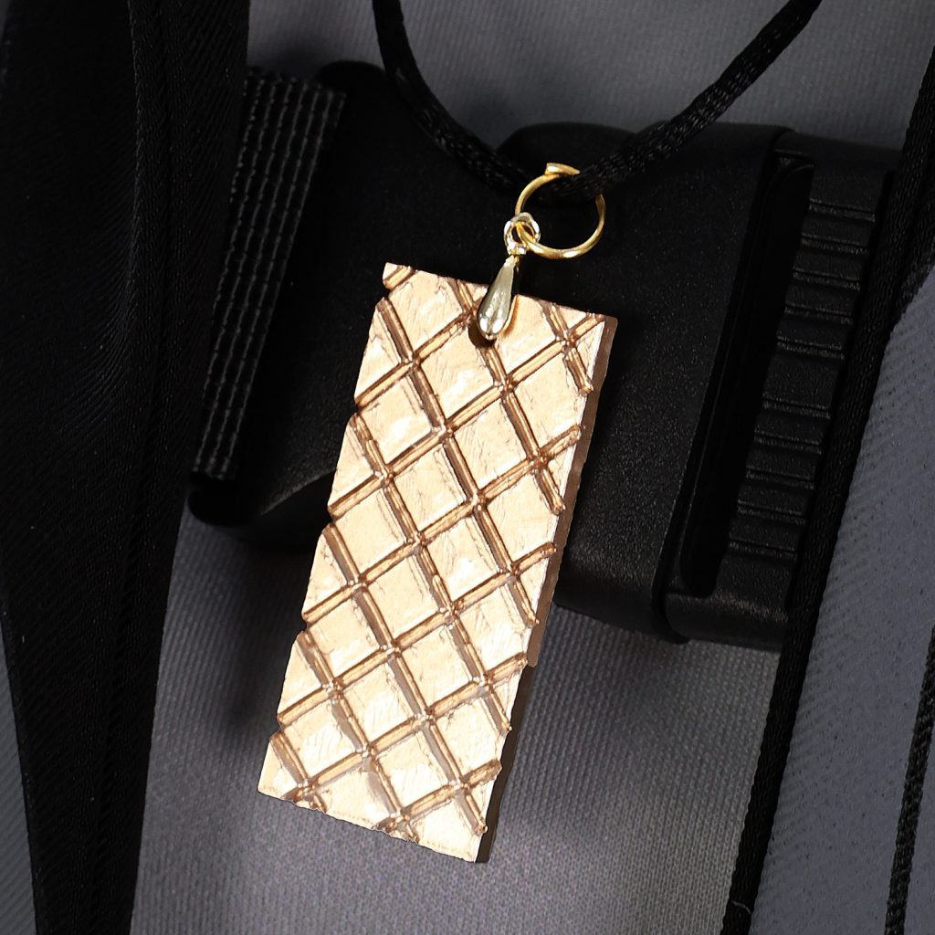 Gold-tone textured pendant against male Rover gray costume top