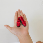 Actual bright red 1:6 figure bow-strap miniature shoe pair with black soles displayed in a hand