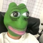 Green frog head mask worn with rounded eyes and pink mouth