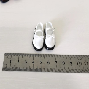 Actual white 1:6 figure bow-strap school-style miniature shoe pair with black trim beside a ruler